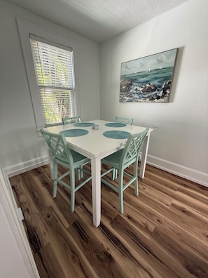 A dining area with a white table, teal chairs, and a painting of a seascape on the wall. - Coastal Cottage / less than 1 mile to Nokomis Beach / Dog-Friendly FENCED YARD (Nokomis)