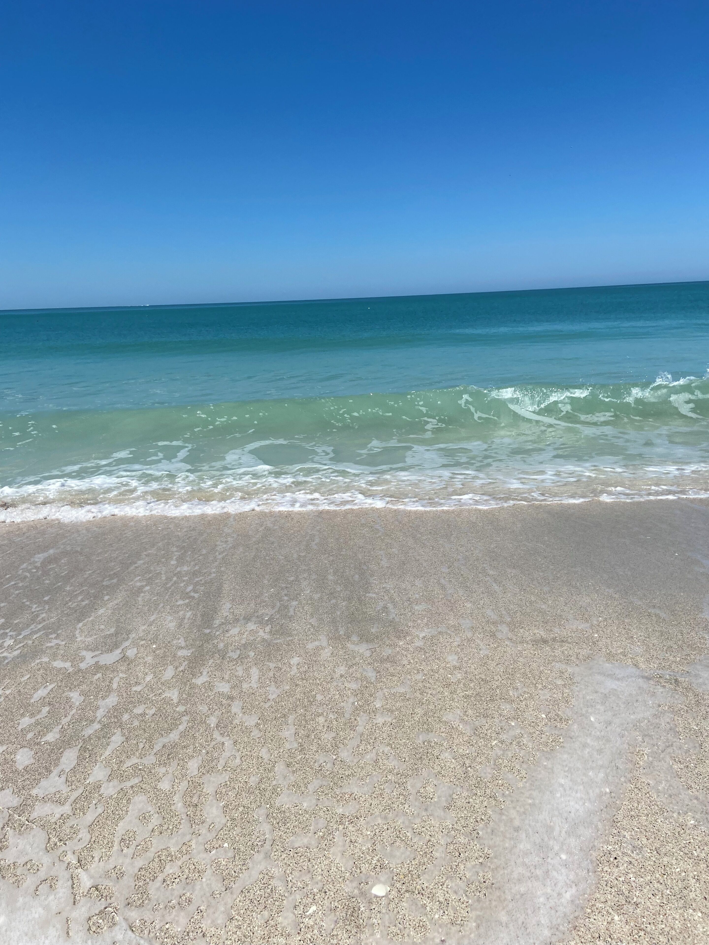 A beach with clear blue water and a sandy shore.