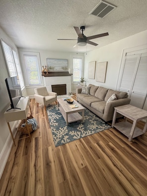 A living room with a fireplace, a ceiling fan, a sofa, a coffee table, and a TV.