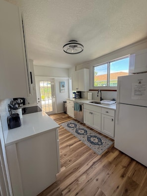 A kitchen with white cabinets, a wooden floor, a ceiling fan, a window, and a refrigerator. - Coastal Oasis / less than 1 mile to Nokomis Beach / Dog-Friendly FENCED YARD (Nokomis)