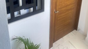 A hallway with a wooden door and a window with a geometric metal grille.