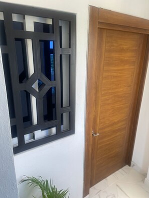 Un pasillo con una puerta de madera y una ventana con una celosía metálica geométrica.