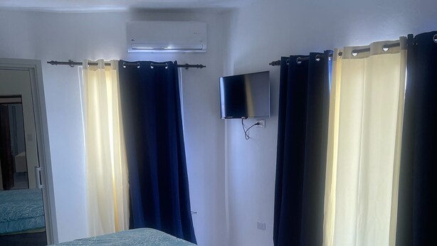 A hotel room with a bed, a TV mounted on the wall, and curtains on the windows.