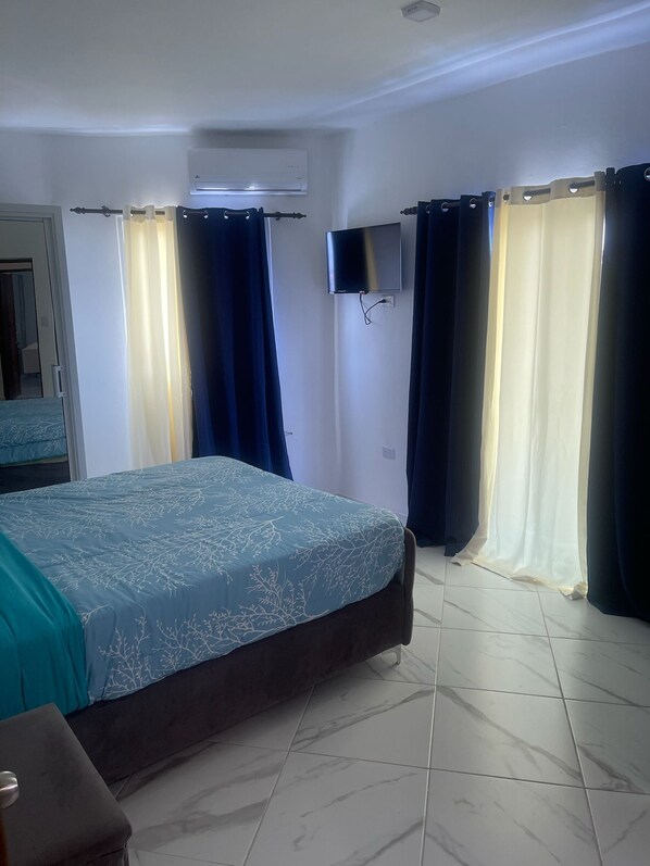 Una habitación de hotel con cama, televisor montado en la pared y cortinas en las ventanas.