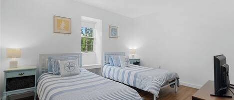 Une chambre avec deux lits, une télévision et une fenêtre.