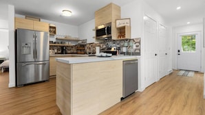 Una cocina moderna con una isla central, electrodomésticos de acero inoxidable, armarios de madera y vistas al exterior.