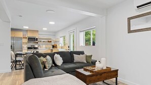 Una sala de estar moderna con un sofá seccional gris, una mesa de centro de madera y una zona de comedor con una mesa y sillas.