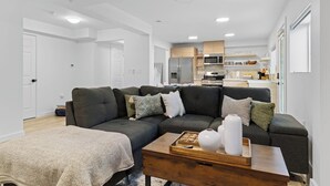 Una sala de estar moderna con un sofá modular, una mesa de centro de madera y una cocina al fondo.