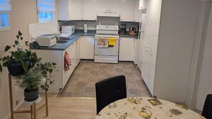 A compact kitchen with white cabinets, a stove, a microwave, and a sink. There is a dining table with chairs and potted plants. - Espace tranquille et accueillante (Repentigny)
