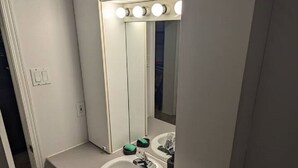 A bathroom with a white sink, a mirror with lights, and a door. - Espace tranquille et accueillante (Repentigny)