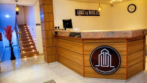 Un espace d’accueil d’hôtel avec un comptoir de réception en bois, une horloge et un panneau indiquant le nom de l’hôtel.
