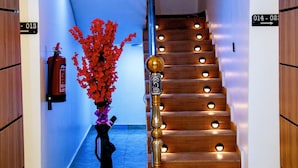 Un escalier dont les marches sont illuminées, un extincteur, un vase rempli de fleurs rouges et une guitare posée sur le sol.