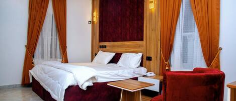 A hotel room with a bed, a wooden nightstand, a red chair, and a window with curtains.