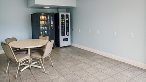 Une pièce avec une table à manger beige et quatre chaises, deux distributeurs automatiques et un mur bleu clair avec des moulures blanches.