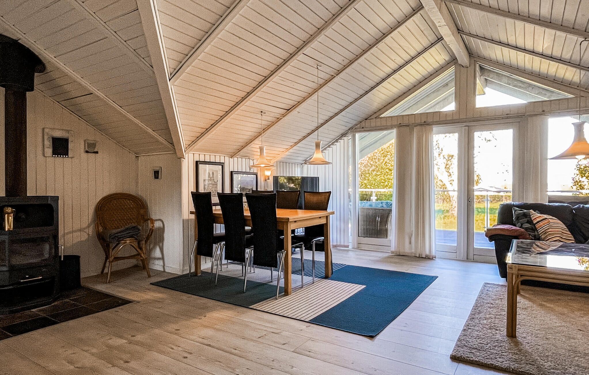 Ein geräumiger Raum mit hoher Decke, Kamin, Essbereich mit Stühlen, einer Couch und einem großen Fenster für natürliches Licht.