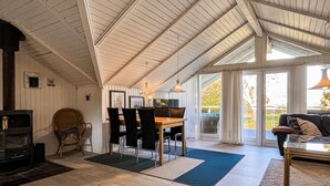 Un'ampia stanza con soffitto alto, camino, zona pranzo con sedie, divano e una grande finestra che offre luce naturale.