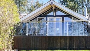 Una casa moderna con rivestimento in legno scuro, una veranda in vetro e un tetto triangolare.