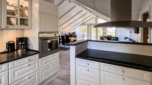 Una cucina con mobili bianchi, forno a incasso e macchina da caffè.