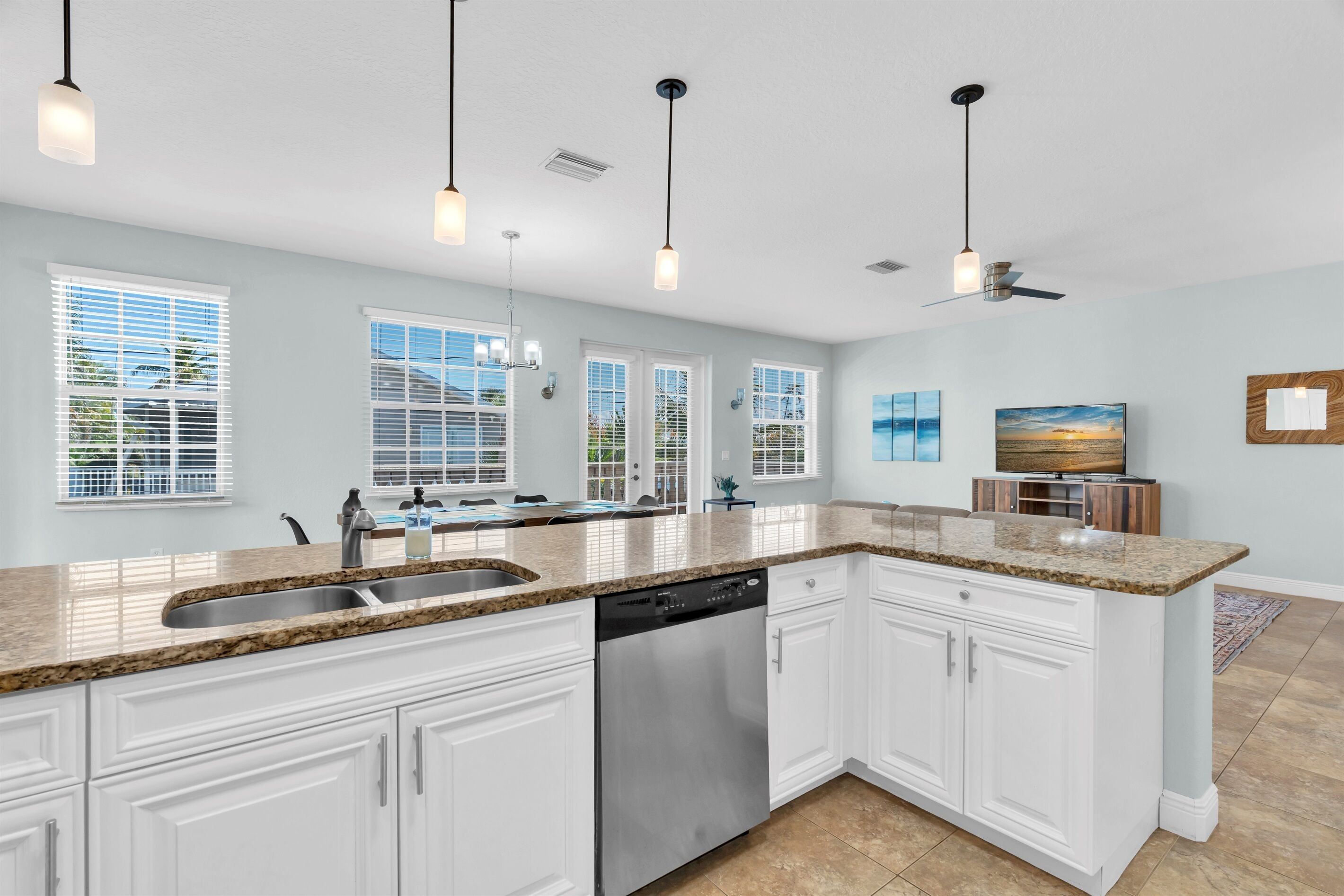 A modern kitchen with white cabinets, granite countertops, a dishwasher, and pendant lighting.