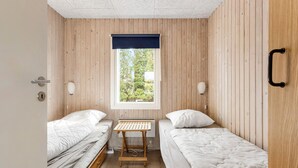 Een kleine, compacte kamer met twee éénpersoonsbedden, een tafeltje en een raam met uitzicht op groen.
