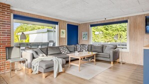 Een moderne woonkamer met een grijze hoekbank, een houten salontafel en een aan de muur bevestigde televisie.