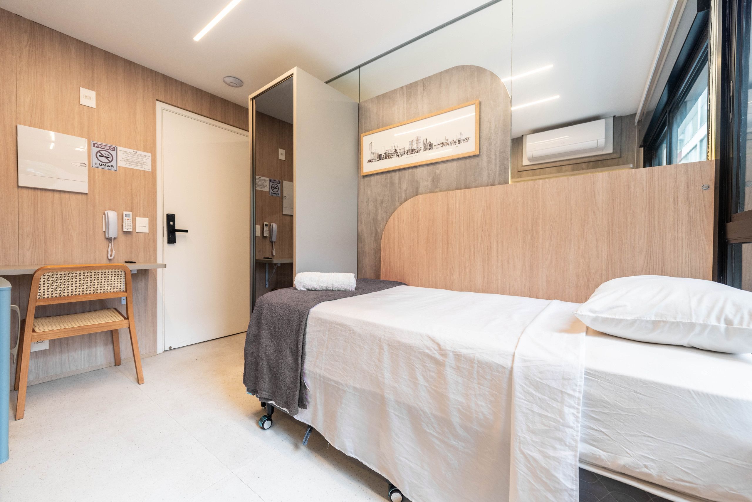 Een hotelkamer met een bed, een bureau, een stoel en een aan de muur bevestigde telefoon.