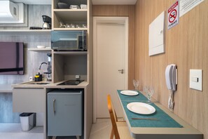 Eine kleine Küche mit Mikrowelle, Kaffeemaschine und einem Kühlschrank. Ein Esstisch ist gedeckt mit Unterlage und Weinglas.