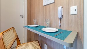 A small dining area with a table set for two, a chair, a phone, and a light switch on the wall. - Melo Alves_31 2p / 1q (São Paulo)