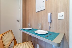 Ein kleiner Essbereich mit einem für zwei Personen gedecktem Tisch, einem Stuhl, einem Telefon und einem Lichtschalter an der Wand.