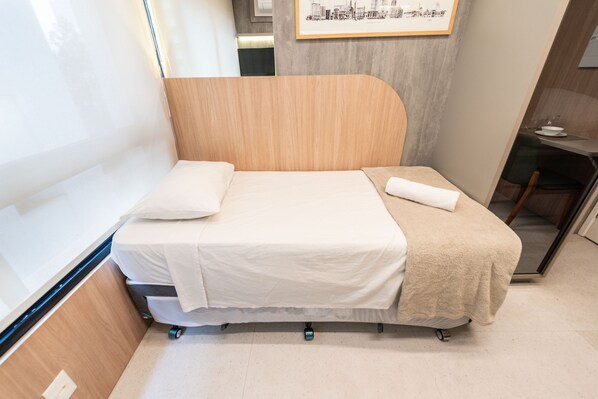 Ein kompaktes Bett mit hölzernem Kopfteil, einer weißen Matratze und einer beigen Decke.