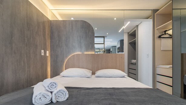Une chambre d’hôtel moderne avec un grand lit, une tête de lit en bois et une armoire intégrée.