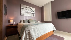 A bedroom with a bed, nightstands, a wall-mounted TV, and a large painting. - Luxury condo with Rooftop pool & Ocean views (Boca de Tomatlán)