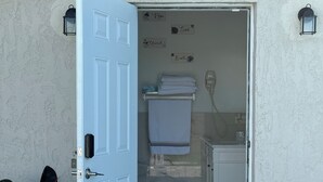 A white door leading to a bathroom with a towel rack, a small plant, and a wall-mounted light fixture. - Modern Private Room -Super Clean and Quiet Stay (Miami)
