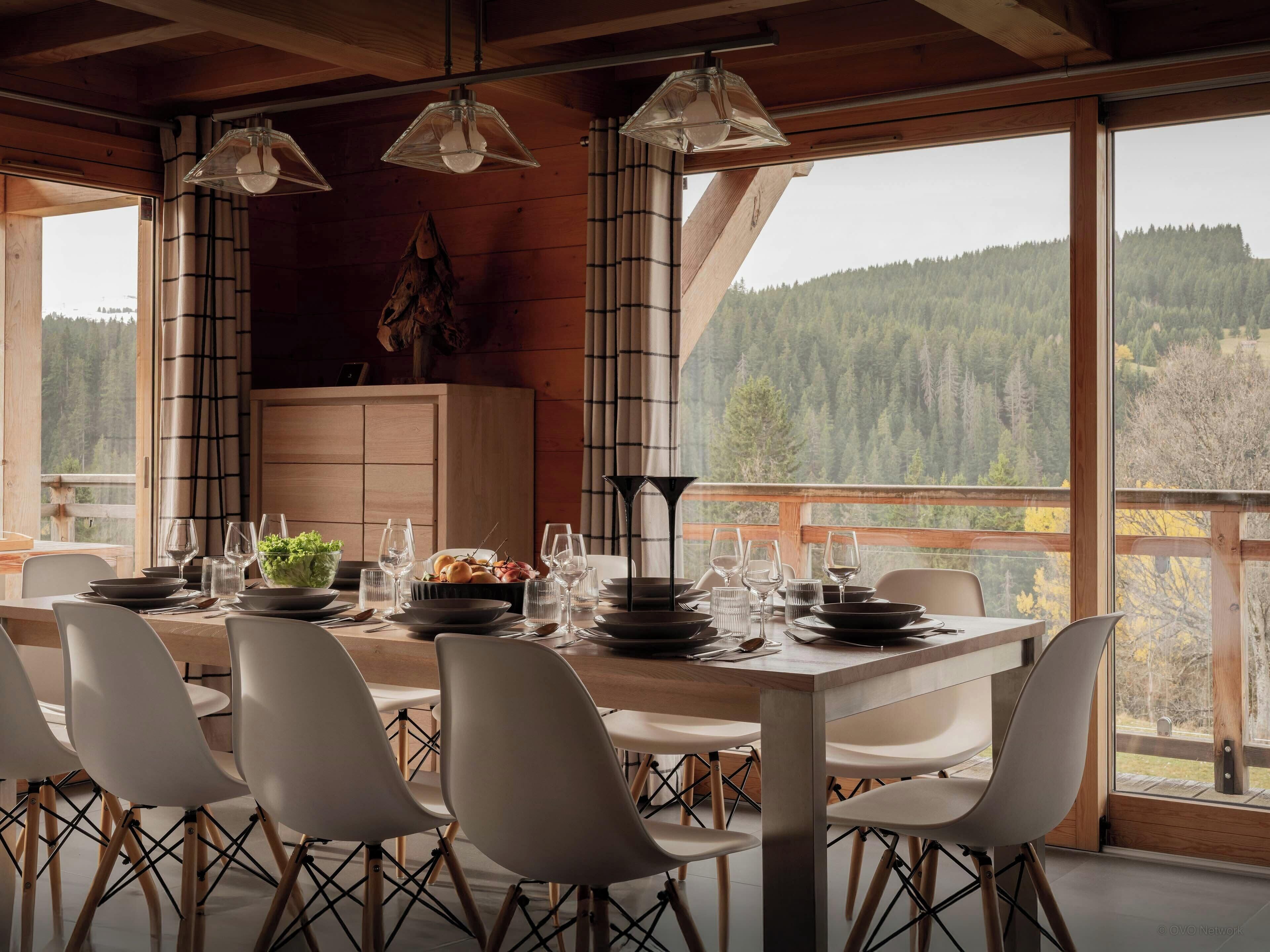 Ein Essbereich mit einem Tisch für sechs Personen, umgeben von Stühlen, mit Blick auf ein bewaldetes Gebirge durch große Fenster.