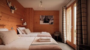 Ein gemütliches Zimmer mit Holzwänden, zwei Betten, einem kleinen Tisch und einem Fenster mit Vorhängen.