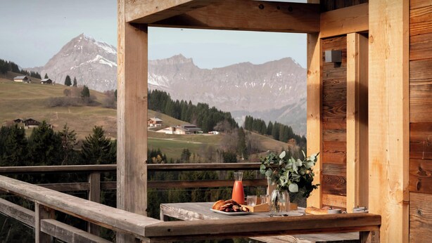 Eine Holzdielen-Terrasse mit einem für das Frühstück gedeckten Tisch, mit Blick auf eine gebirgige Landschaft.