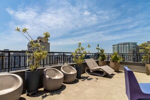Terraço no telhado com espreguiçadeiras, vasos com plantas e vista para a cidade.