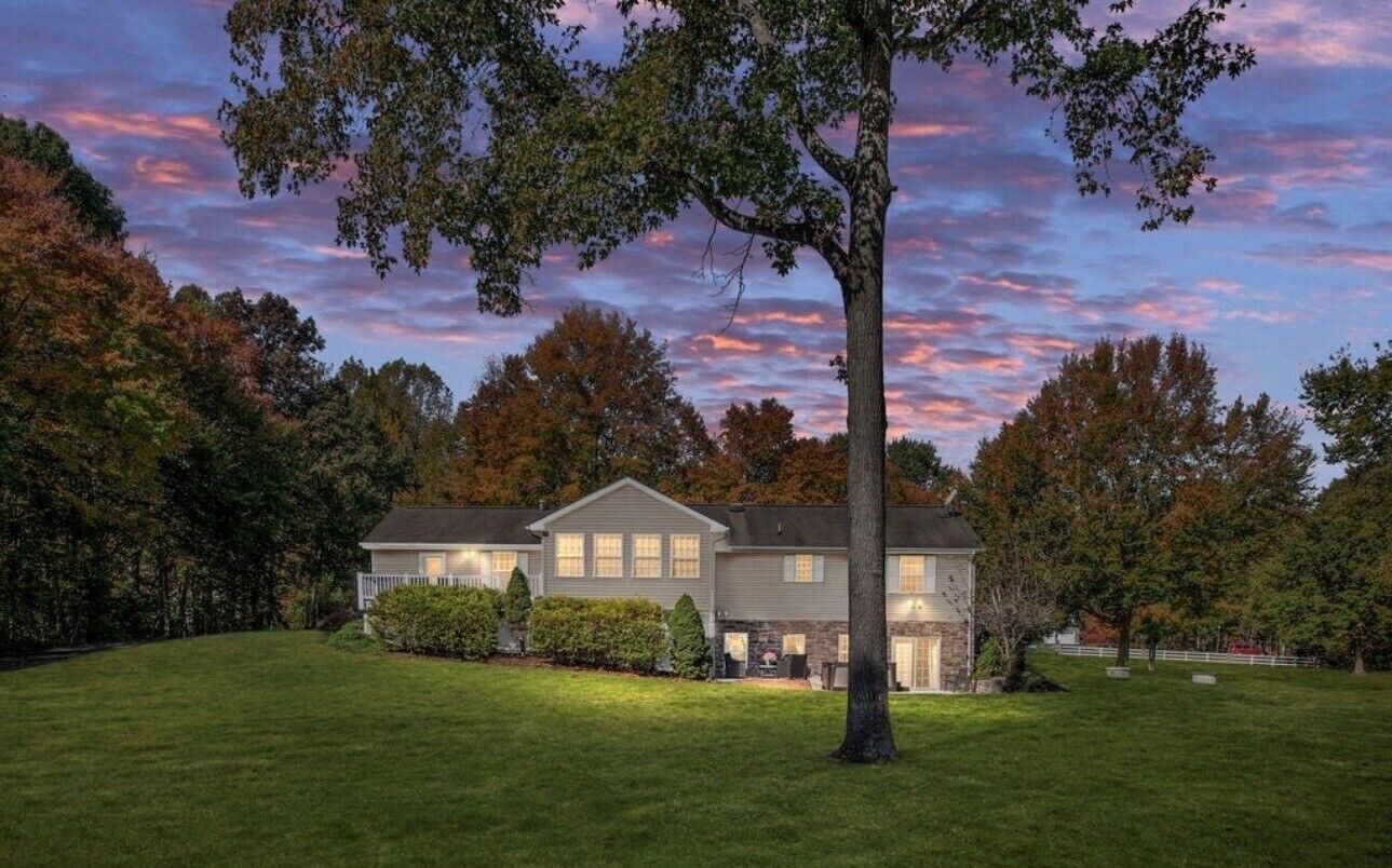 A two-story house with a well-maintained lawn and a large tree in the foreground.