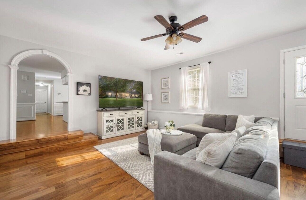 Un salon avec un canapé gris, un ventilateur de plafond, un téléviseur à écran plat et un plancher en bois.