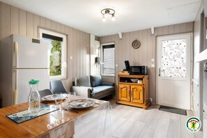 A compact kitchen with a refrigerator, microwave, and wooden cabinets. There is a dining table set with plates and glasses. - Gîtes de France® - La Maison au Calme (CRIEL SUR MER)