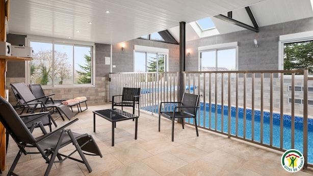 A modern indoor pool area with a view of the pool, sun loungers, and a glass-enclosed balcony. - Gîtes de France® - Villa des Champs (VILLERS SOUS FOUCARMONT)