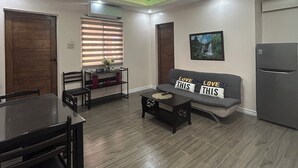 A modern living room with a dining area, a ceiling fan, and a refrigerator.