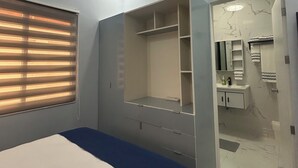A bedroom with a bed, a ceiling fan, an air conditioning unit, a window with blinds, and a bathroom with a sink and mirror.