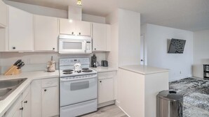 Una cocina compacta con armarios blancos, un microondas, un horno y un lavabo.
