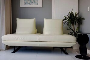 A modern living room with a white sofa, a potted plant, and a black table.