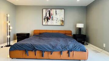 A modern bedroom with a large bed, a floor lamp, a side table, and a wall-mounted abstract painting.