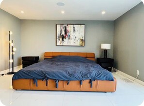 A modern bedroom with a large bed, a floor lamp, a side table, and a wall-mounted abstract painting.