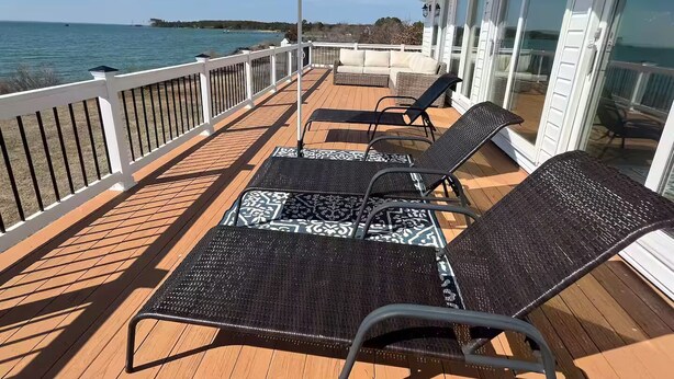 Um terraço com duas cadeiras de descanso e um guarda-sol listrado, com vista para um corpo de água.