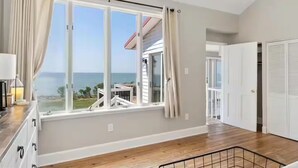 Quarto espaçoso com grande janela e vista para o mar, piso de madeira e porta branca.