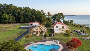 Uma piscina com um deck ao redor, uma área de estar coberta ao ar livre e um edifício com telhado vermelho.